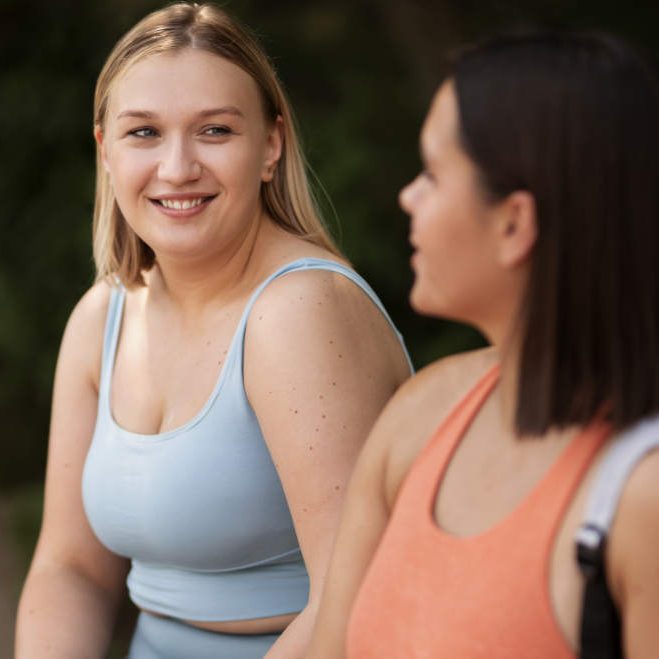Abnehmkurs in Hamburg Zwei Frauen in Sportkleidung unterhalten sich lächelnd im Freien.
